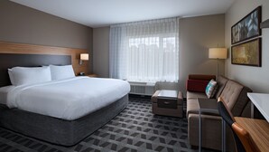 Habitación de hotel con una cama grande, un sofá, un escritorio y una ventana con cortinas translúcidas.