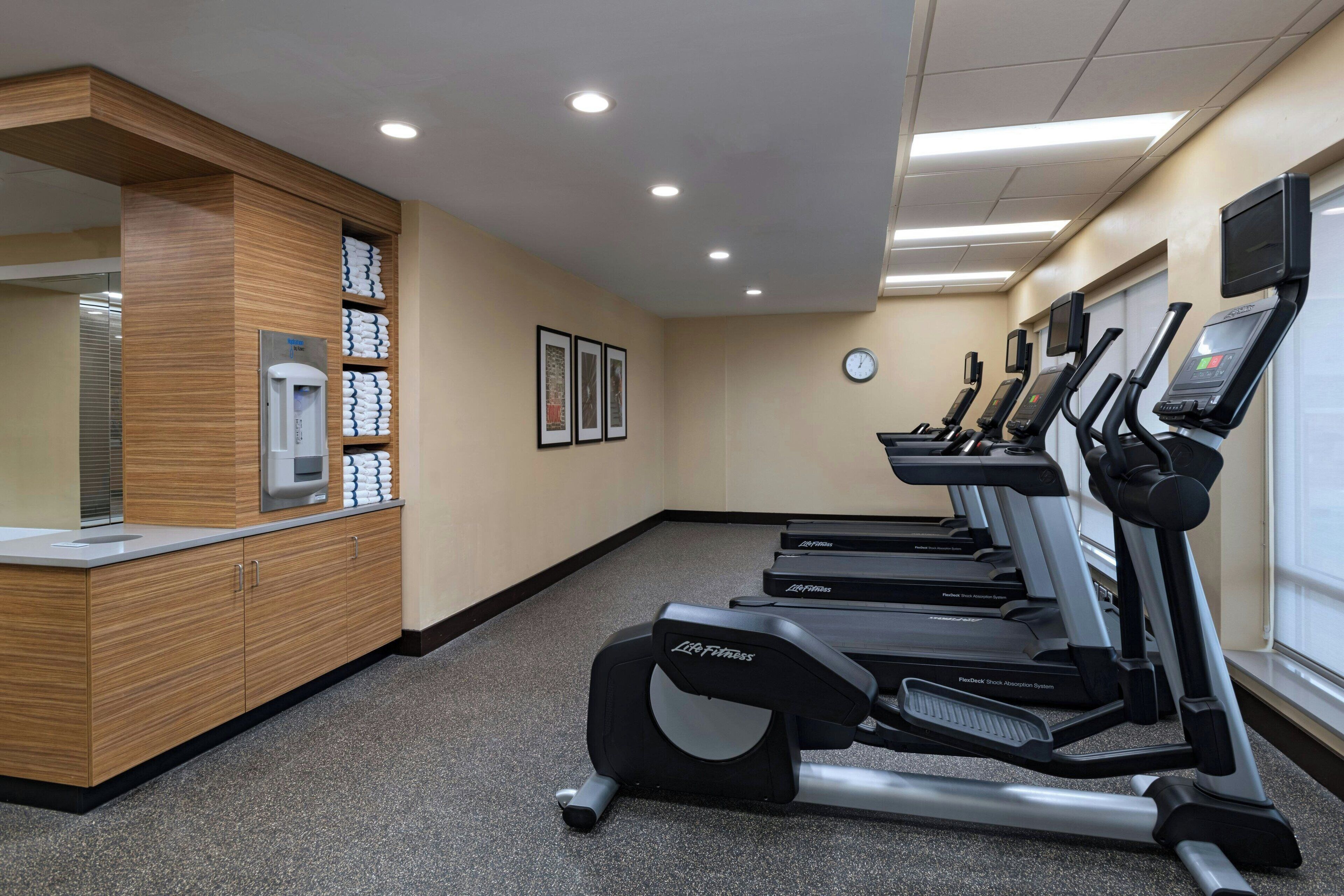 A fitness center with treadmills, a water dispenser, and a wooden vanity with towels.