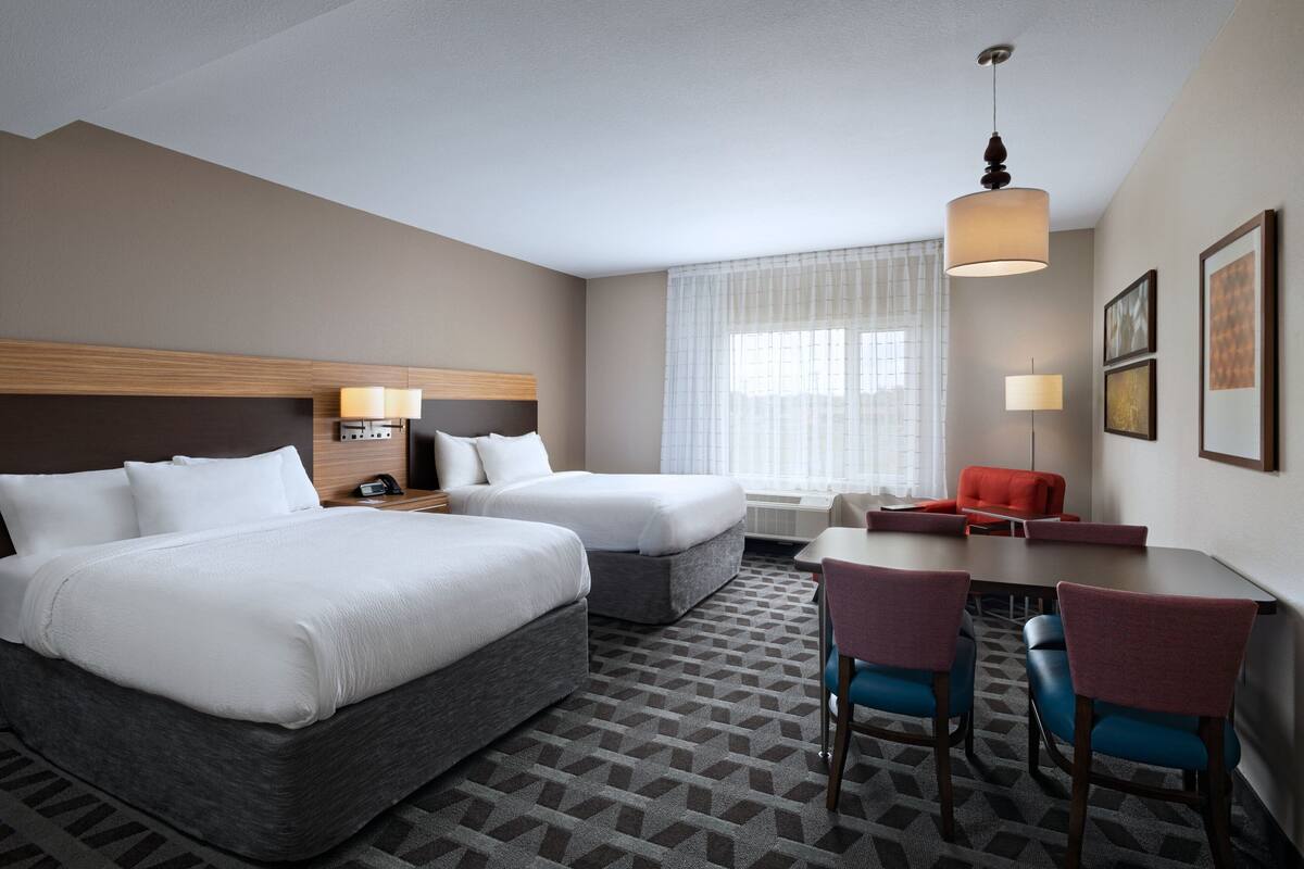 Una habitación de hotel con dos camas, un escritorio, sillas, una lámpara y una ventana con cortinas.