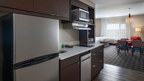 Cocina compacta con refrigerador, microondas y lavavajillas. Cuenta con un comedor con mesa y sillas, y una ventana con cortinas.