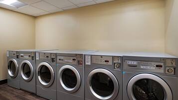 A row of front-loading washing machines in a laundry room with beige walls and a wooden floor.