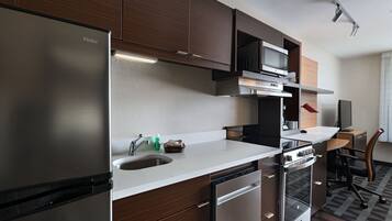 Cocina moderna con refrigerador de acero inoxidable, microondas y horno. Cuenta con un lavamanos con grifo, encimera y una silla.