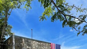 A stone building with a large American flag, parked cars, and a clear blue sky. - Historical Hotel, Main Street Blowing Rock (Blowing Rock)
