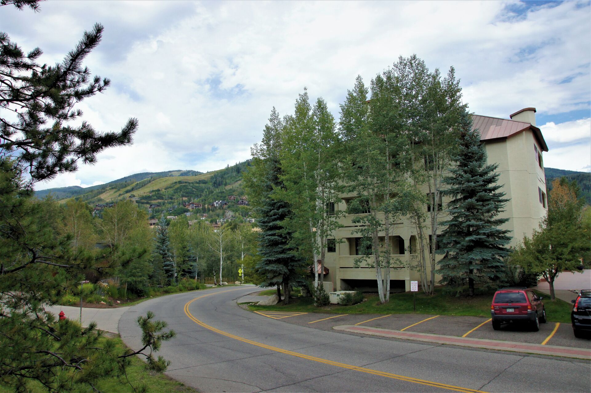 A building with a curved driveway, surrounded by trees and a mountainous backdrop.