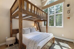 A bedroom with a wooden four-poster bed, a window with a view of trees, and a small stool.