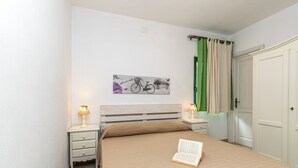 A bedroom with a bed, a nightstand with a lamp, a wall-mounted artwork, and a door with a green curtain. - Domos Pintadas Apt. 4 Porto Rotondo (Olbia)