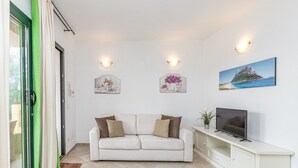 A living room with a white sofa, a flat-screen TV, and wall-mounted light fixtures. - Domos Pintadas Apt. 4 Porto Rotondo (Olbia)