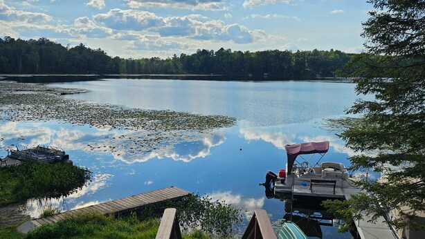 A wooden dock leading to a calm lake with a boat and a covered area. - Cozy cabin on Island Lake (Winter)