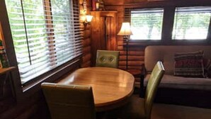 A cozy cabin interior with a wooden dining table and chairs, a sofa, and large windows with blinds. - Cozy cabin on Island Lake (Winter)