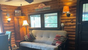 A cozy log cabin interior with a sofa, a ceiling fan, and a sign reading "The Flavor of the Northwoods." - Cozy cabin on Island Lake (Winter)