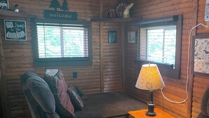 A cozy cabin-style room with a sofa, a chair, a lamp, and a window with blinds. - Cozy cabin on Island Lake (Winter)