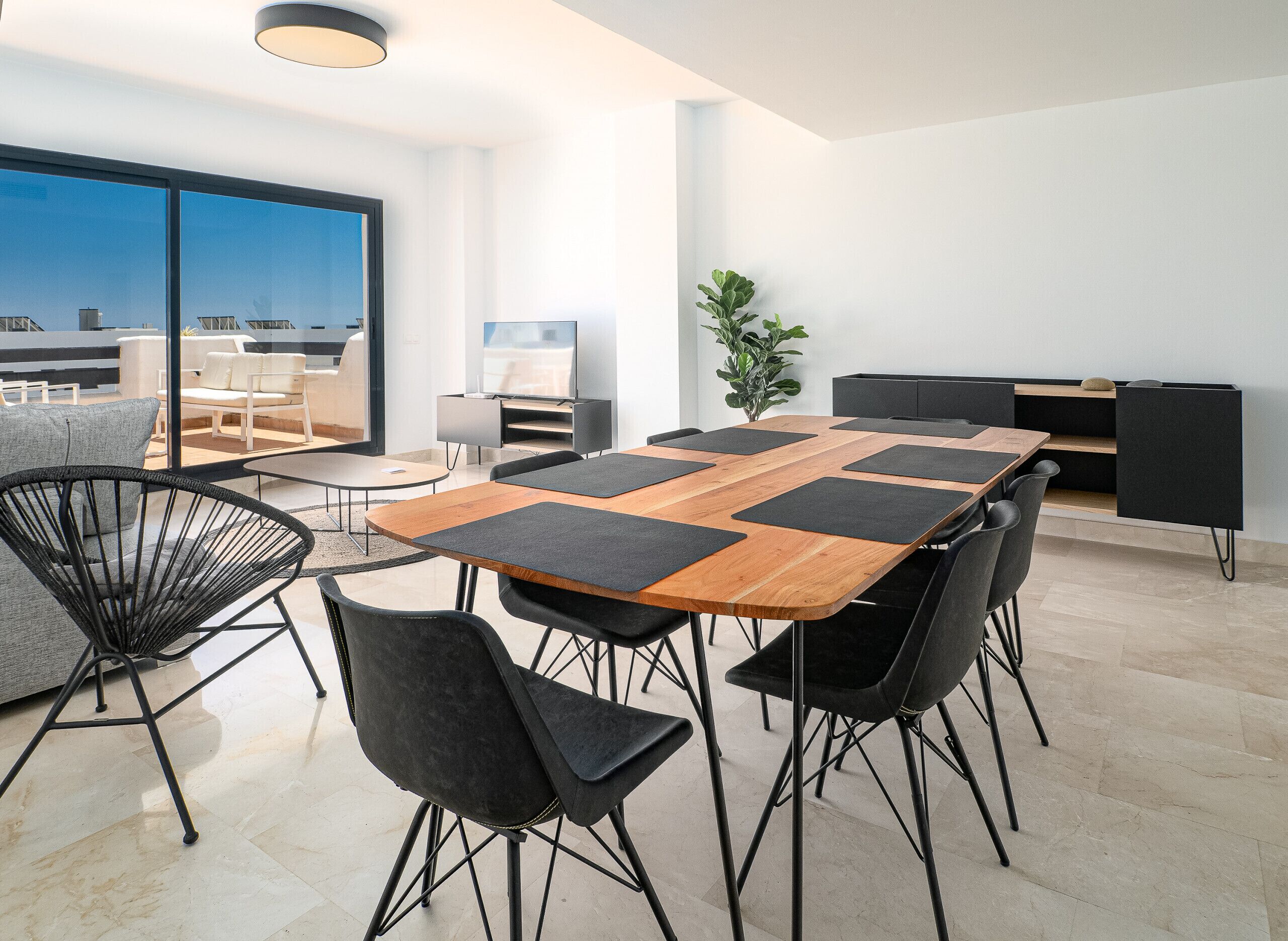 A modern dining area with a large table, black chairs, and a plant.