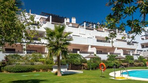 A white building with multiple balconies, a swimming pool, and lush greenery. - Lotus 2341 Golf beach & pool (Casares)