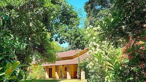 A rustic building with a tiled roof, surrounded by lush greenery and a dirt path leading to the entrance. - Recanto da Serra do Mendanha (RJ)