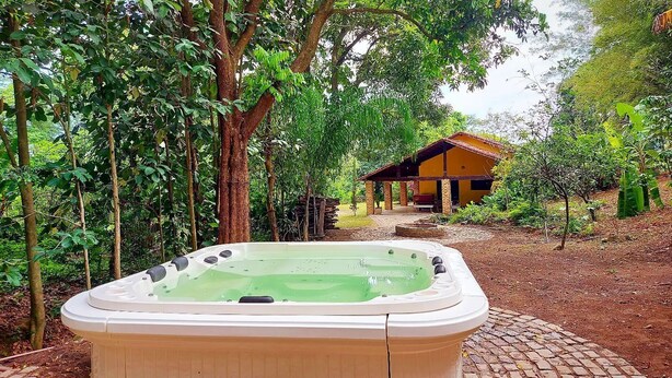 A hot tub in a lush garden with a wooden building in the background. - Recanto da Serra do Mendanha (RJ)