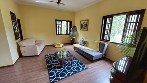 A living room with a sofa, a chair, a coffee table with flowers, a patterned rug, and a large window with a view of greenery. - Recanto da Serra do Mendanha (RJ)