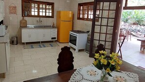 A kitchen with white cabinets, a yellow refrigerator, and a stove. There is a table with a lace tablecloth and a vase of flowers. - Recanto da Serra do Mendanha (RJ)