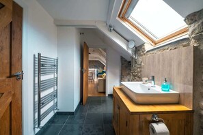A modern bathroom with a skylight, a wooden vanity, and a stone accent wall. - Stunning Converted Granary in Heart of St Davids (St Davids)