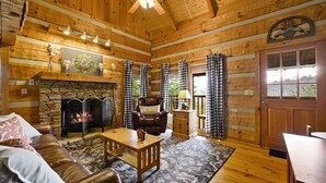 A cozy cabin interior with a stone fireplace, leather sofa, and checkered curtains. - Free Dollywood Tix/VIEWS/Couples Cabin/HotTub/ (Sevierville)