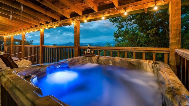 A hot tub under a wooden pergola with string lights, surrounded by a wooden deck and overlooking a mountainous landscape. - Free Dollywood Tix/VIEWS/Couples Cabin/HotTub/ (Sevierville)