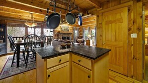 A wooden cabin kitchen with a central island, hanging pots, and a stone fireplace. - Free Dollywood Tix/VIEWS/Couples Cabin/HotTub/ (Sevierville)
