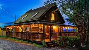 A wooden cabin with a porch, large windows, and string lights. - Free Dollywood Tix/VIEWS/Couples Cabin/HotTub/ (Sevierville)