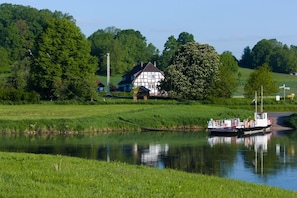 A riverside view with a traditional house, a boat, and lush greenery.