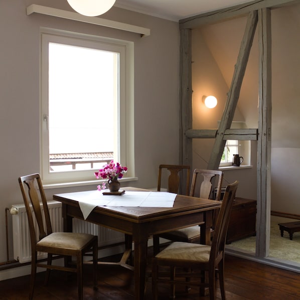 A dining area with a table, chairs, a vase of flowers, and a window with a view.