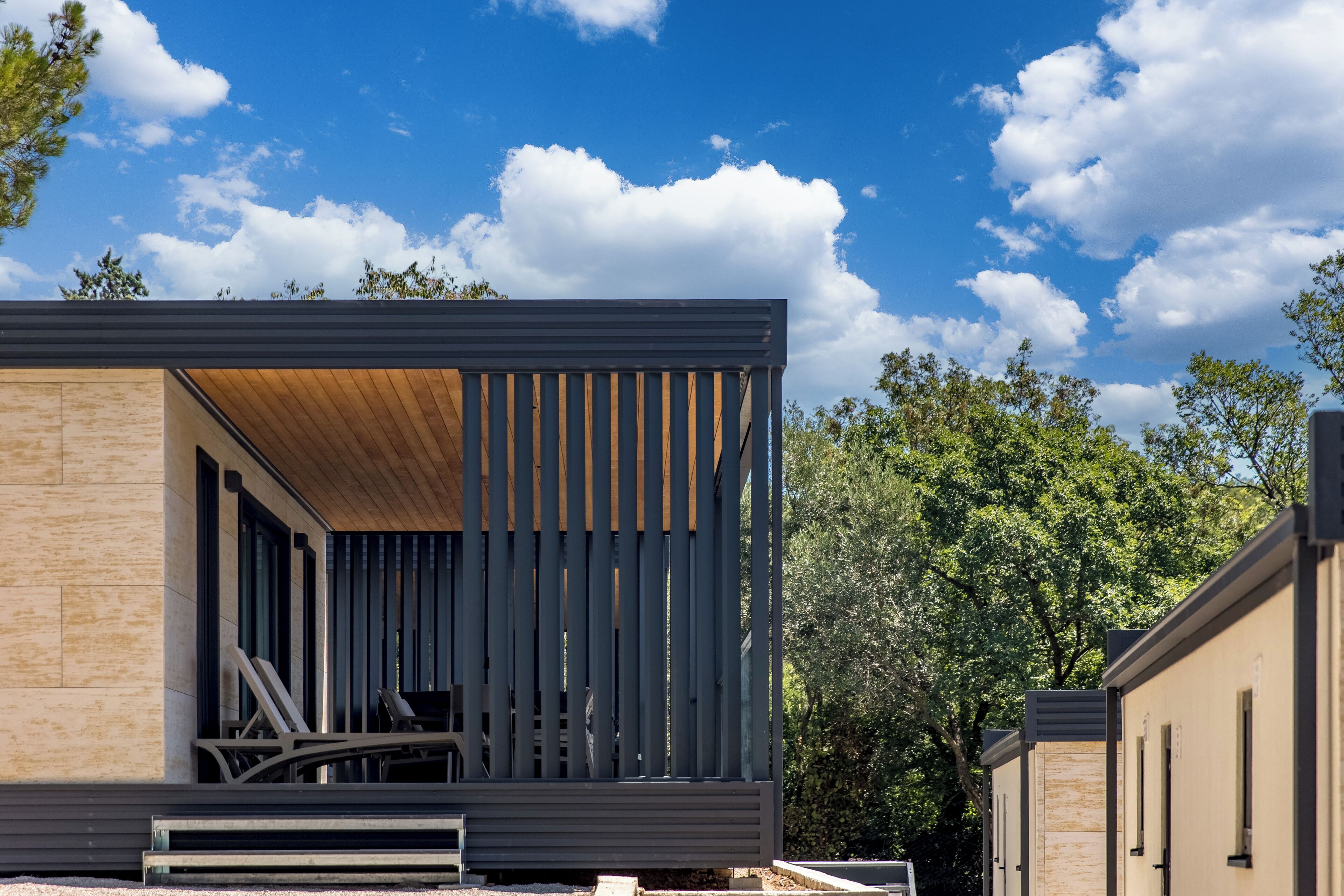A modern building with a wooden slatted roof and beige walls, featuring a covered outdoor seating area.