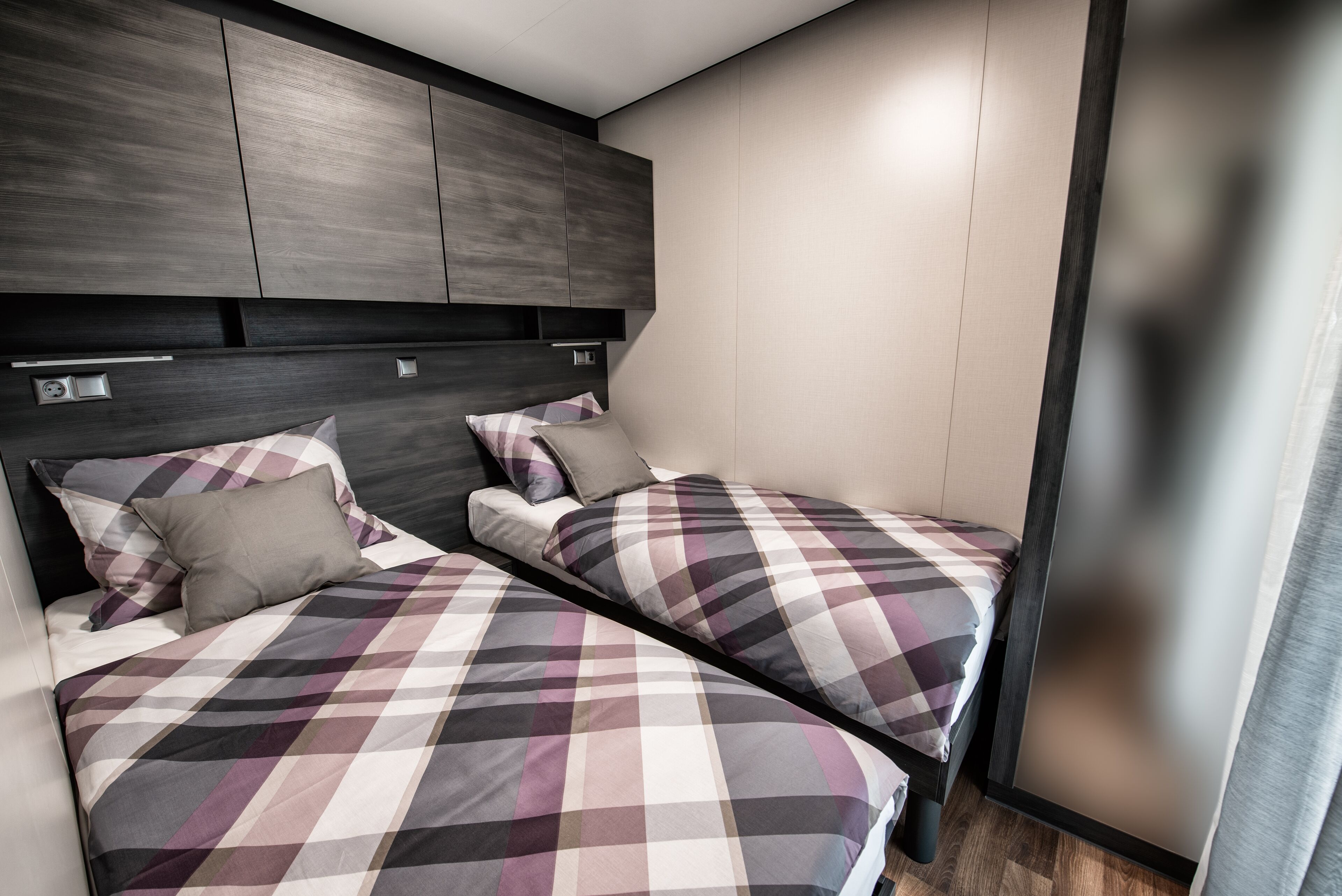 Une chambre moderne avec deux lits, une tête de lit sombre et une palette de couleurs neutres.