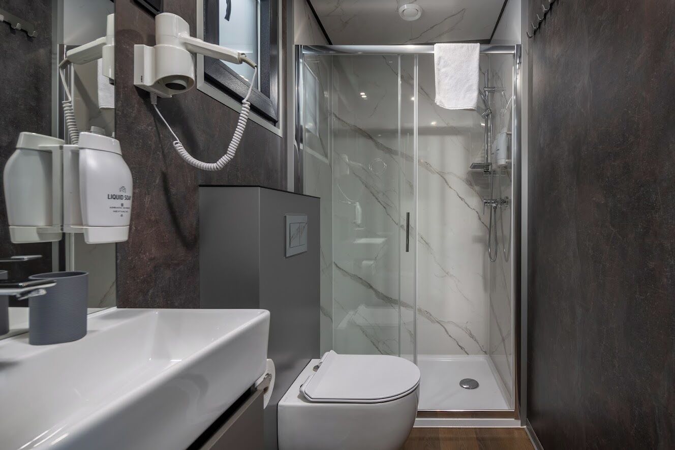 Ein modernes Badezimmer mit Duschabtrennung aus Glas, einer weißen Toilette und einem Waschtisch mit Spiegel und Fön.