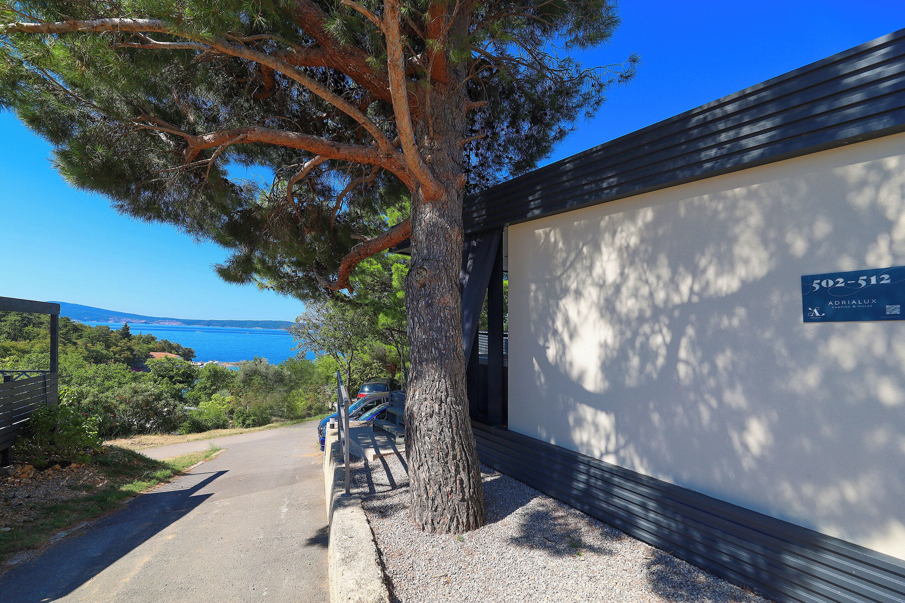 A tree-lined driveway leading to a building with a sign reading "502-512 ABRIELLA".