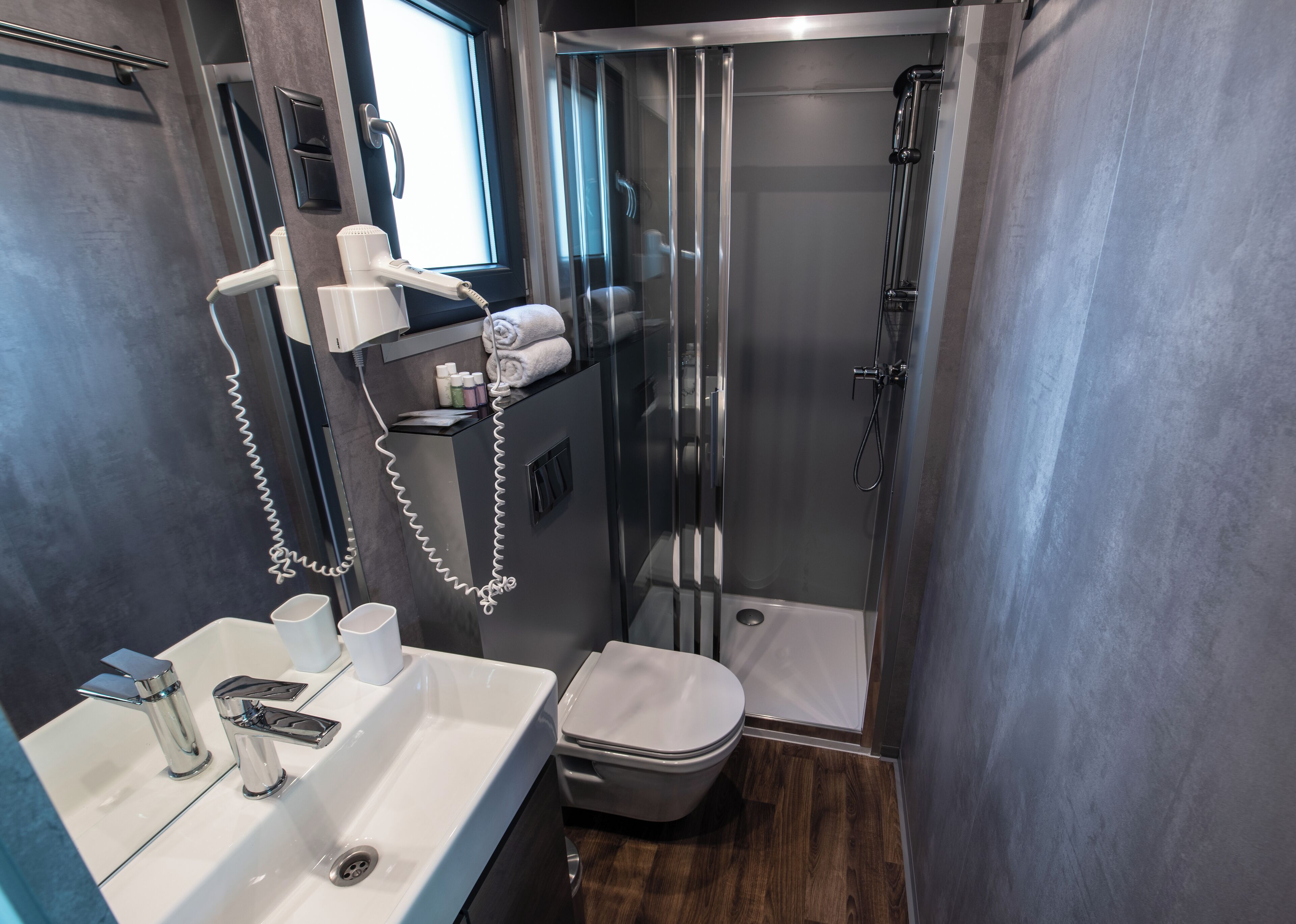 A compact bathroom with a glass-enclosed shower, a white sink with modern faucets, and a toilet.