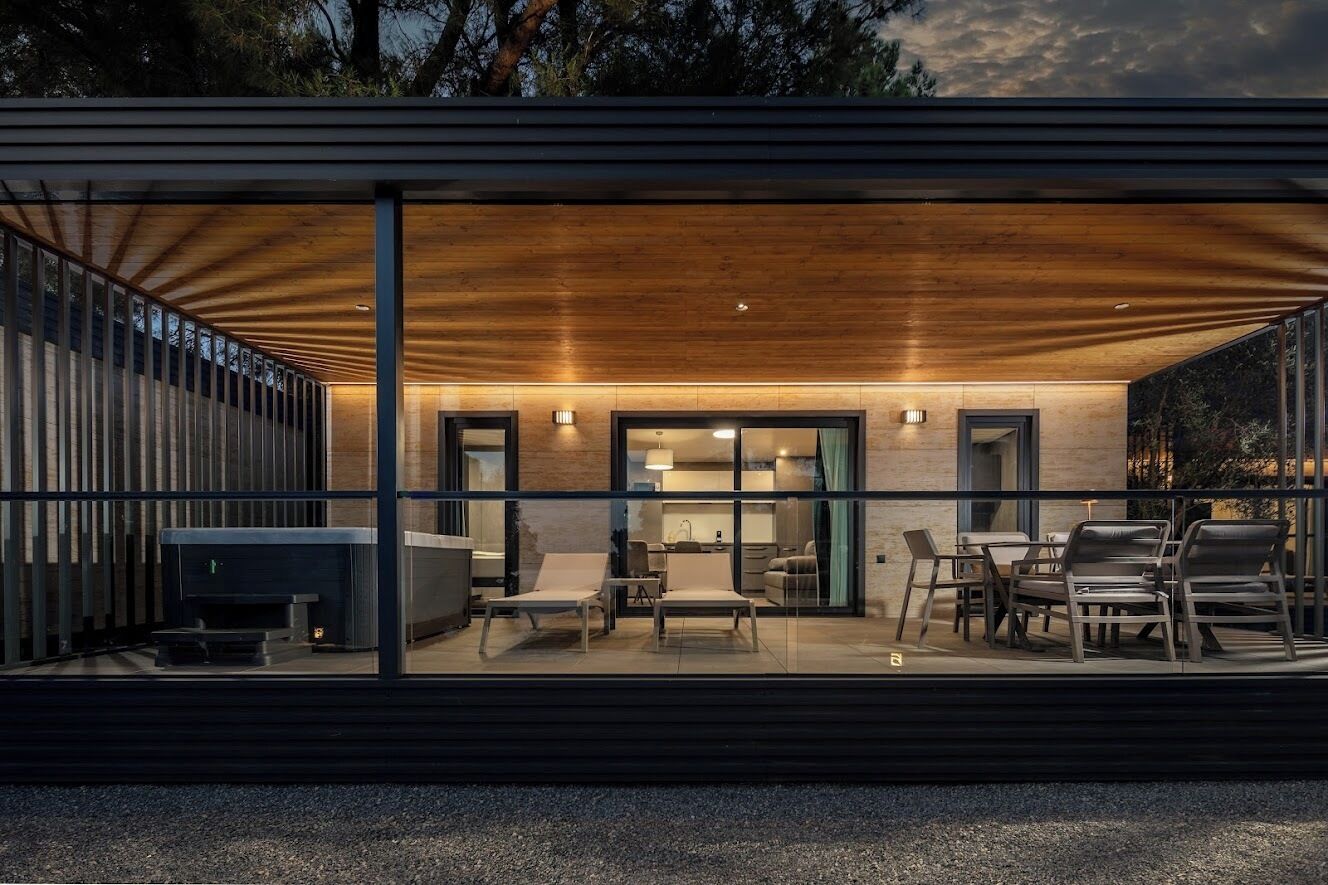 Een modern huis met een overdekte patio, inclusief een open haard, zitplaatsen en een keuken die zichtbaar is door grote glazen deuren.