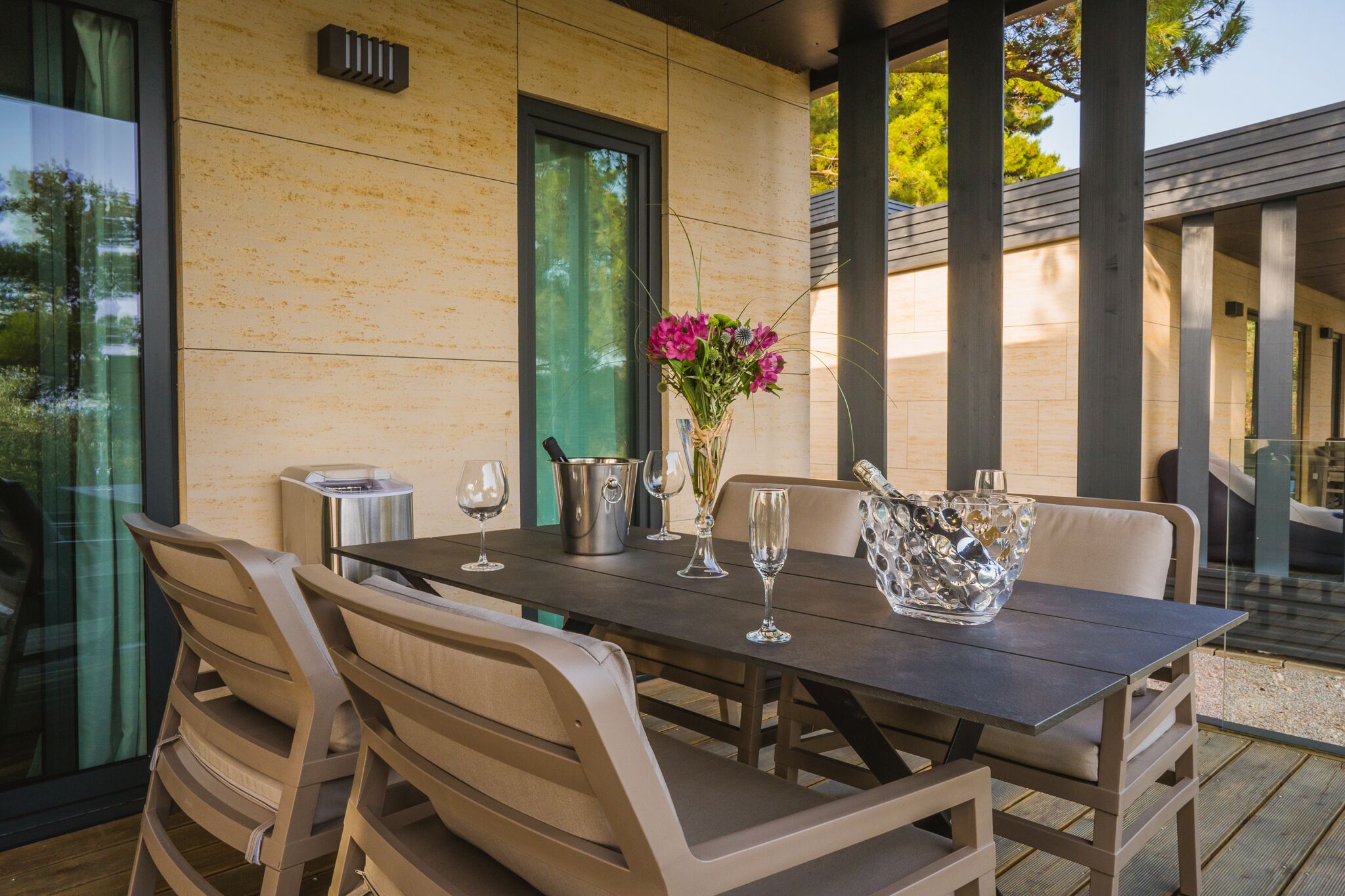 An outdoor dining area with a table set for two, a vase with flowers, and a metal bucket.
