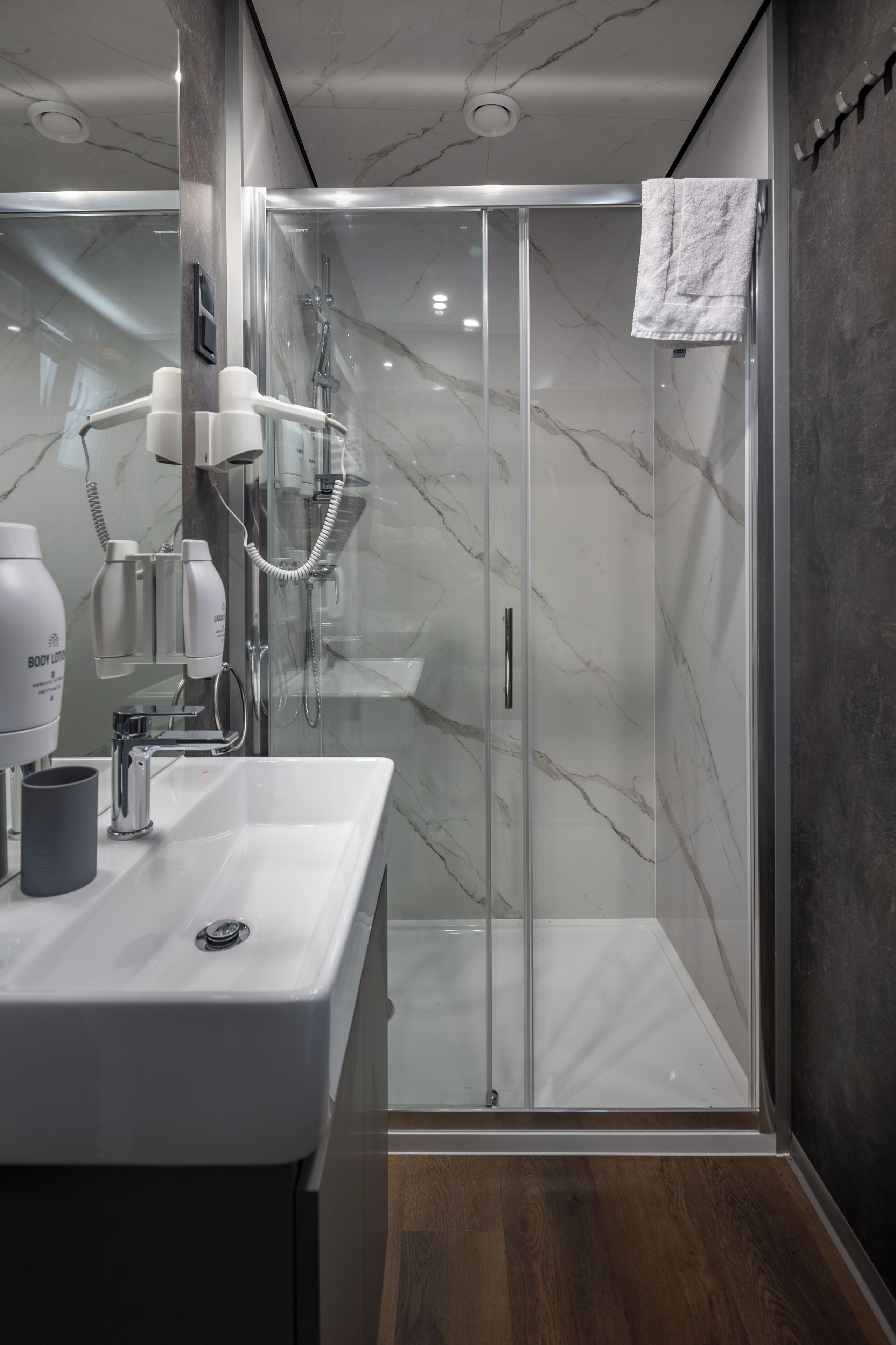 A modern bathroom with a glass-enclosed shower, a white sink, and a hairdryer on the counter.