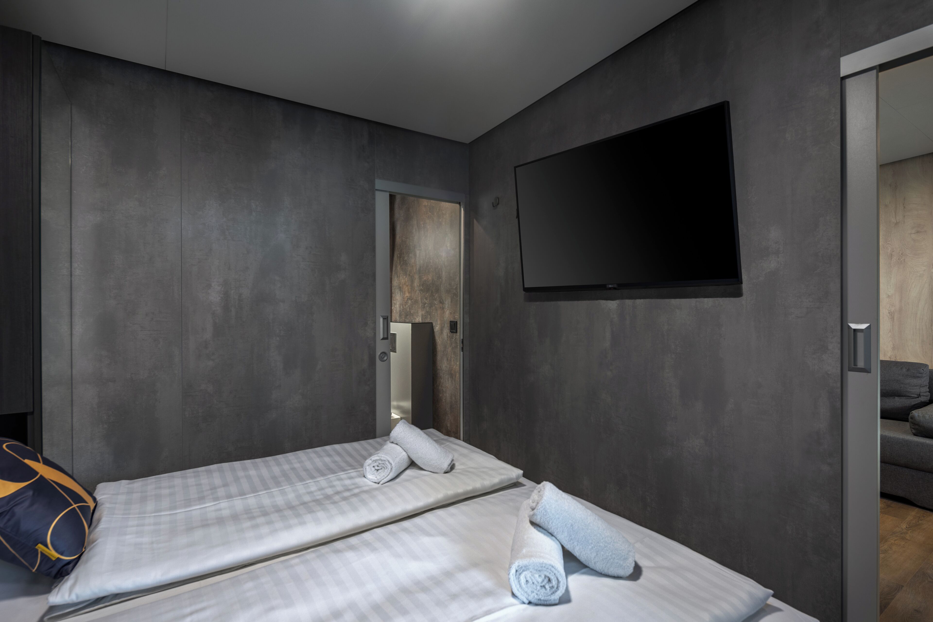 Ein modernes Hotelzimmer mit zwei Betten, einem wandmontierten Flachbildfernseher und einer Holztür.