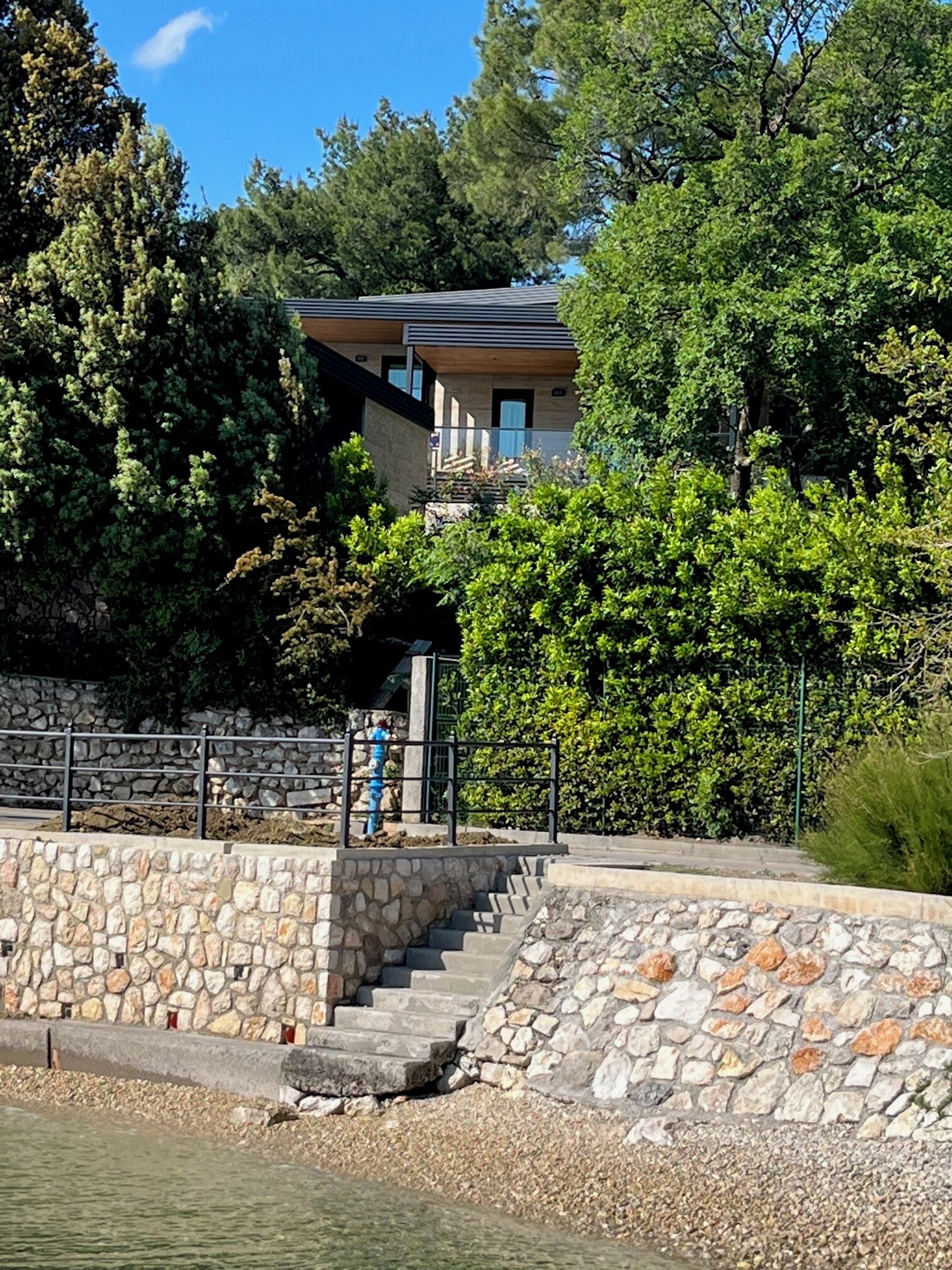 Ein modernes Gebäude mit einer Steinstufe, die zu einem Balkon führt, umgeben von üppigem Grün und einer Steinmauer.