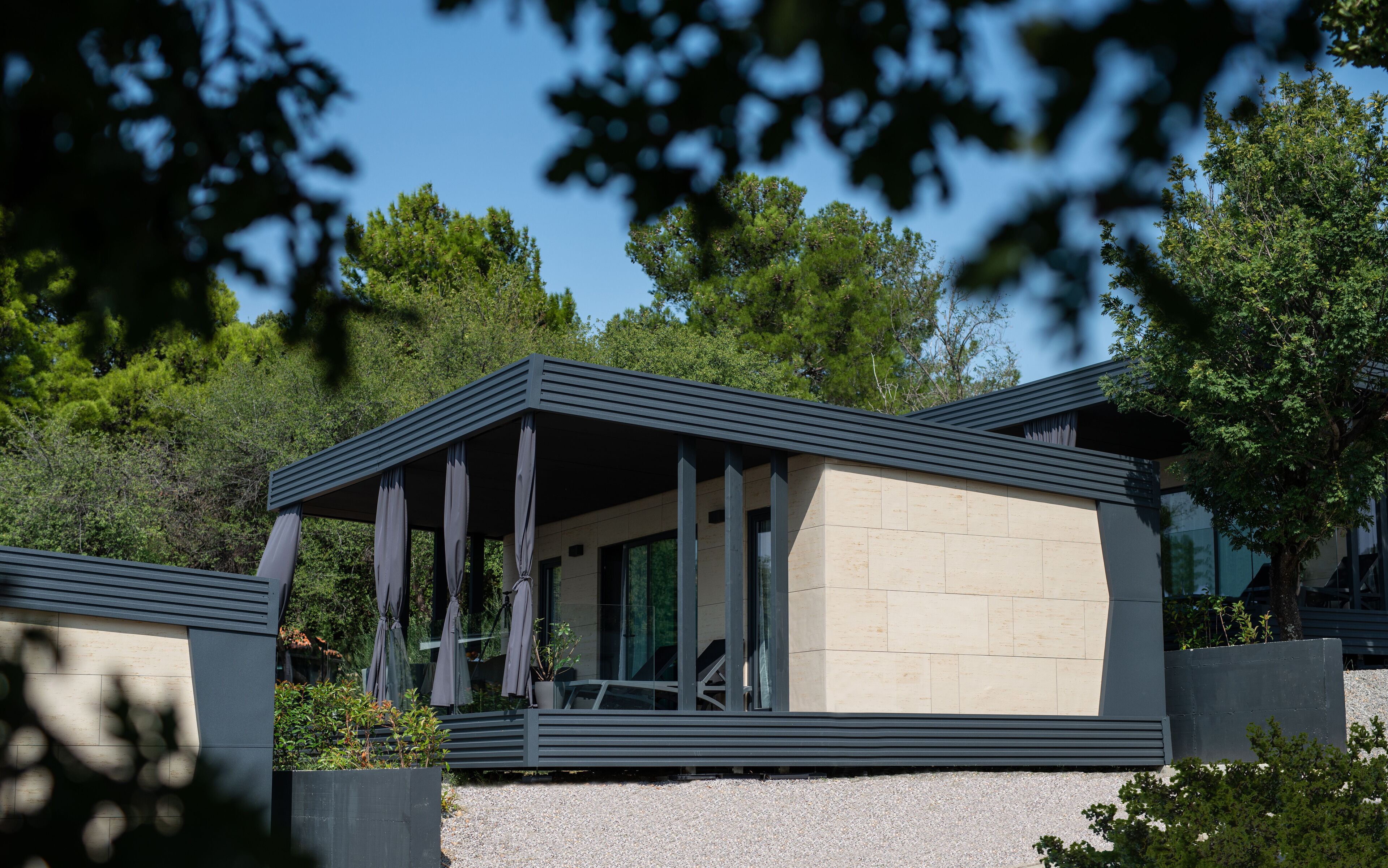 A modern building with a flat roof, large windows, and a covered outdoor area with seating.