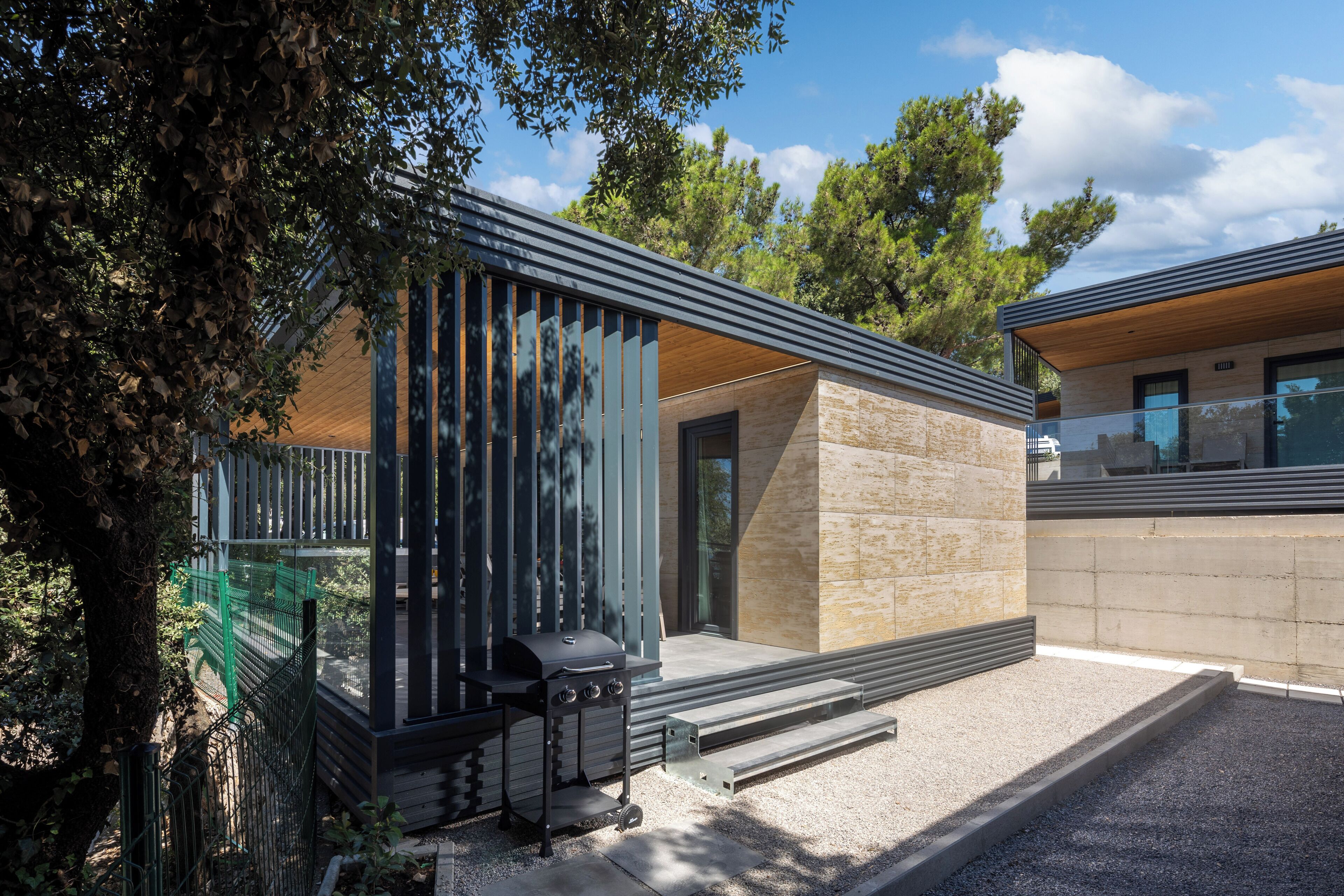 A modern house with a patio, a grill, and a view of trees.