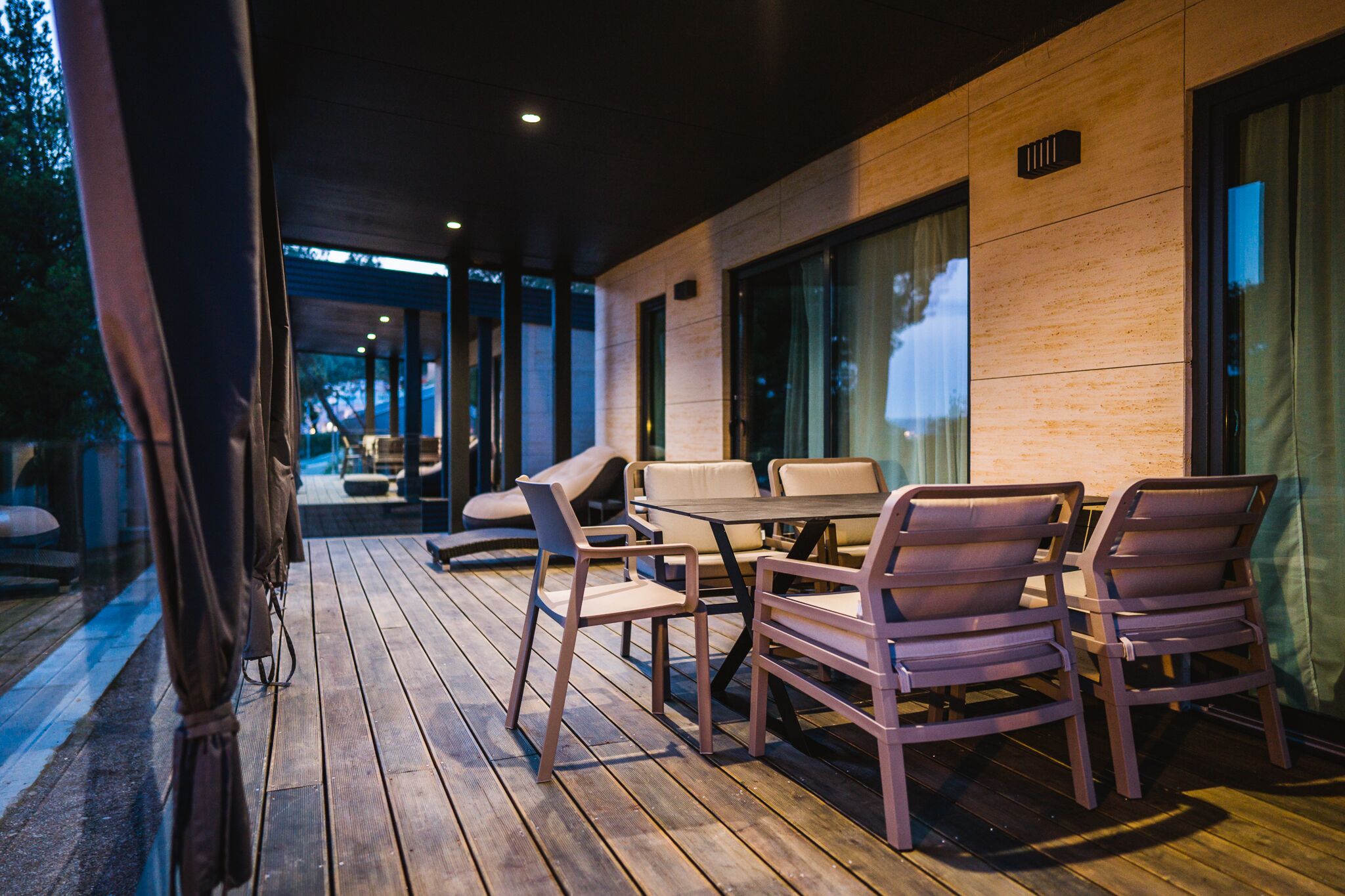 Um pátio externo com piso de madeira, uma mesa e cadeiras.