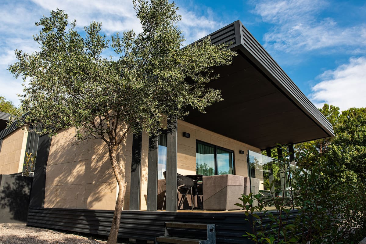 A modern building with a flat roof, large windows, and a covered outdoor seating area with steps leading up to it.