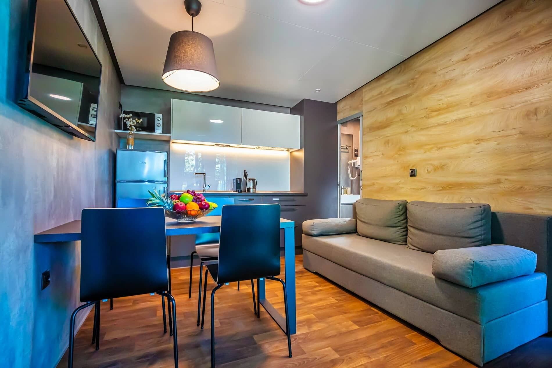 Un espacio habitable moderno con una pared de acento de madera, un sofá, una zona de comedor con sillas y una cocina al fondo.