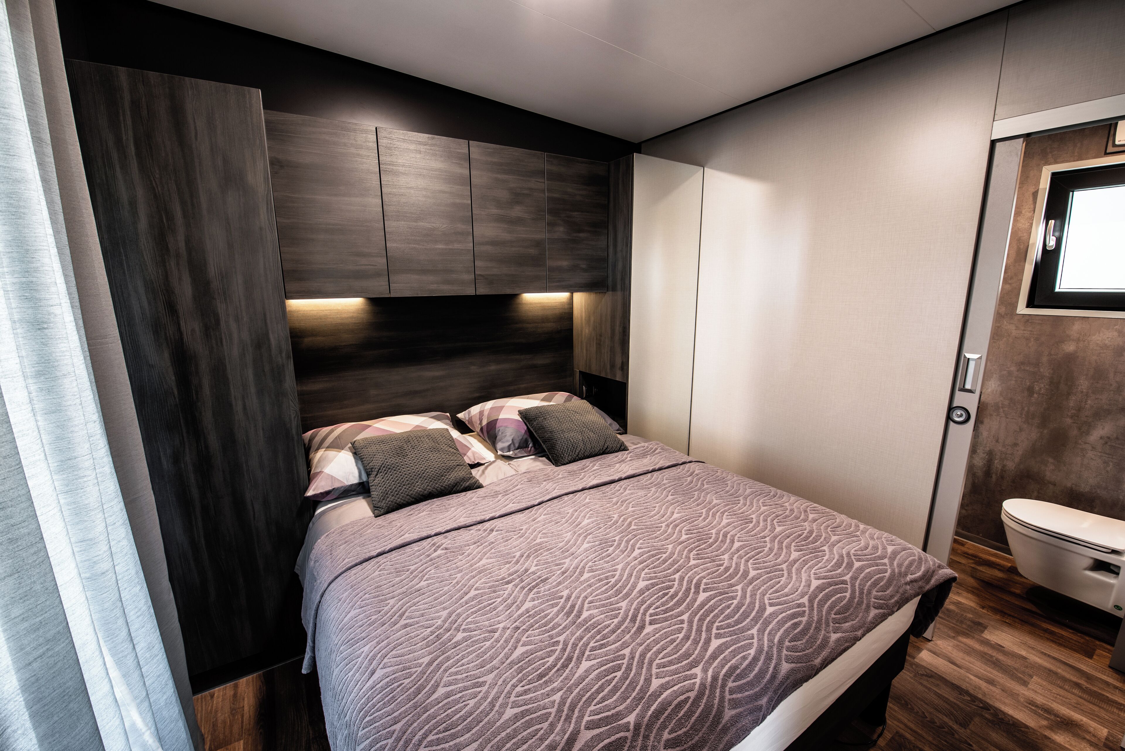 A modern bedroom with a large bed, dark wood headboard, and a built-in wardrobe.