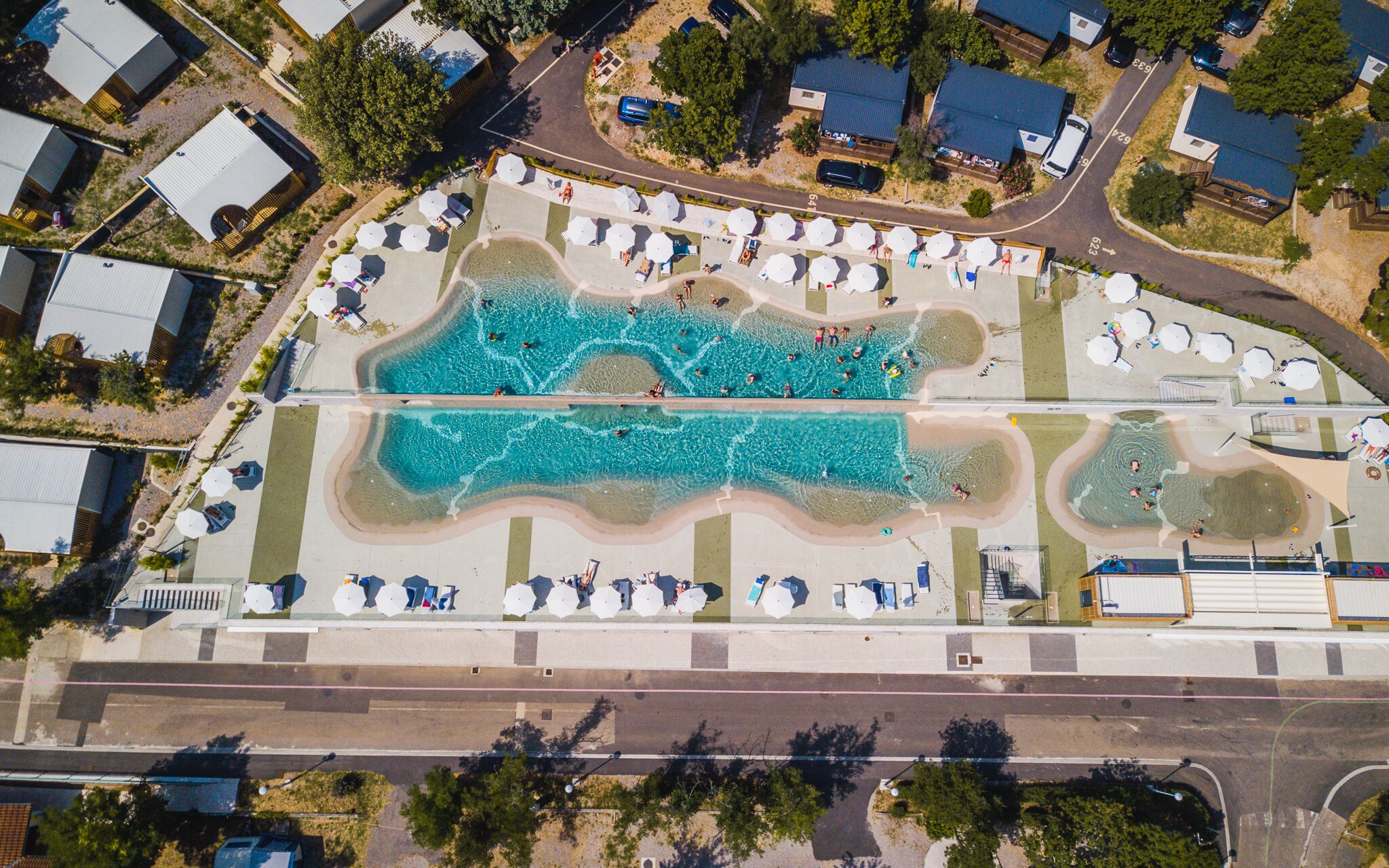 Vista aérea de um resort com uma grande piscina, várias áreas de praia e diversos guarda-sóis.