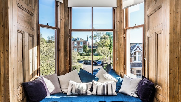 A wooden-framed bay window with a cushioned bench, pillows, and a view of a residential street. - Charming and comfortable apartment, centrally located with easy parking access. Sleeps 4 (North Berwick)