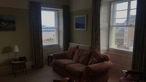 A living room with a sofa, a chair, a lamp, and a view of the outside through large windows. - Perfectly located for town and beach - Victorian terraced house near East Beach. Sleeps 7 (North Berwick)