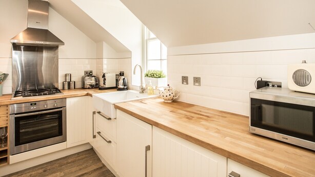 A modern kitchen with white cabinetry, a stainless steel range hood, a built-in oven, a microwave, and a wooden countertop. - Stylish first-floor apartment with private patio, just moments from the High Street. Sleeps 2 (North Berwick)