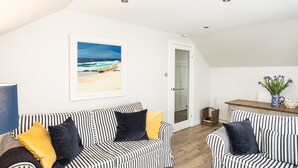 A living room with striped sofas, a framed beach picture, and a wooden coffee table with a vase of flowers. - Stylish first-floor apartment with private patio, just moments from the High Street. Sleeps 2 (North Berwick)