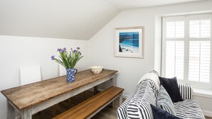 A cozy room with a wooden bench, a table with a vase of flowers, a framed picture on the wall, and a window with blinds. - Stylish first-floor apartment with private patio, just moments from the High Street. Sleeps 2 (North Berwick)
